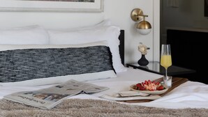 A neatly made bed with white and black pillows, a tray with strawberries and a glass of orange juice, and a newspaper on the bed.