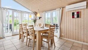 A dining area with a wooden table and chairs, large windows, and an air conditioning unit on the wall.