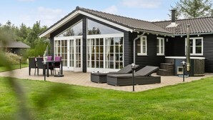 A modern log cabin with a glass-enclosed patio, outdoor seating, and a hot tub.
