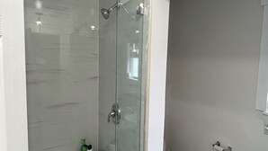 Une salle de bain moderne avec une douche à parois de verre, des toilettes et une petite étagère contenant des articles de toilette.