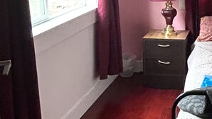 Une chambre avec une fenêtre, une table de chevet avec une lampe, un lit et une commode.