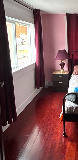 A bedroom with a window, a bedside table with a lamp, a bed, and a nightstand.