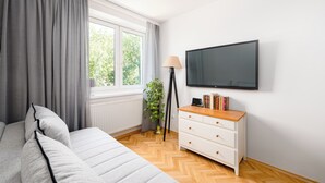 Et soveværelse med seng, kommode, fjernsyn og et vindue med gardiner.
