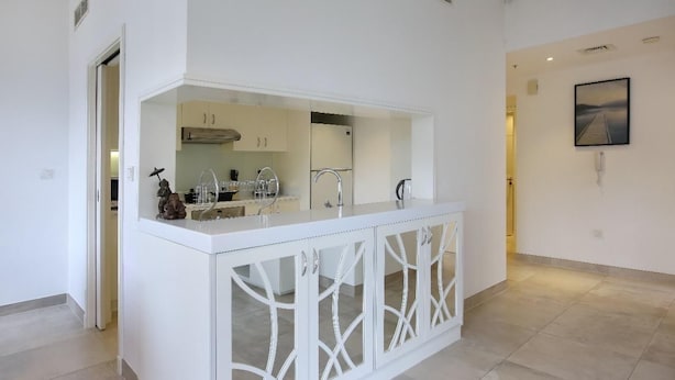 A modern kitchen with white cabinetry, a central island, and a view of the adjacent living area. - Bluewaters Islands Hostel (Dubai)