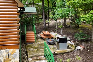 A wooden cabin with a stone foundation, a green porch, a wooden table and bench, and a fire pit area. - The Ginger Fox Log Cabin w/ Resort Perks | Lake Lure (Lake Lure)
