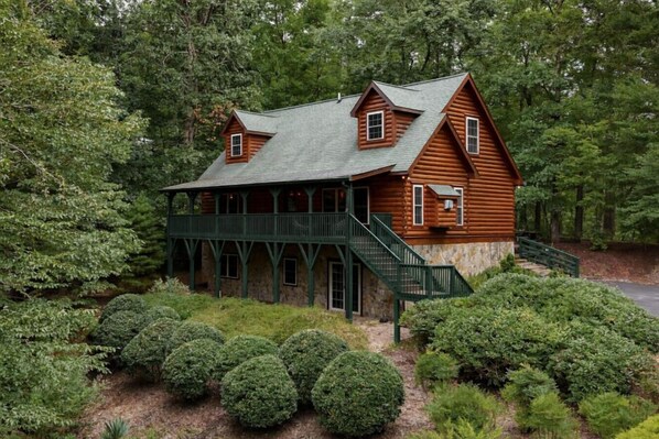 A log cabin with a porch, a staircase, and a view of the surrounding forest. - The Ginger Fox Log Cabin w/ Resort Perks | Lake Lure (Lake Lure)