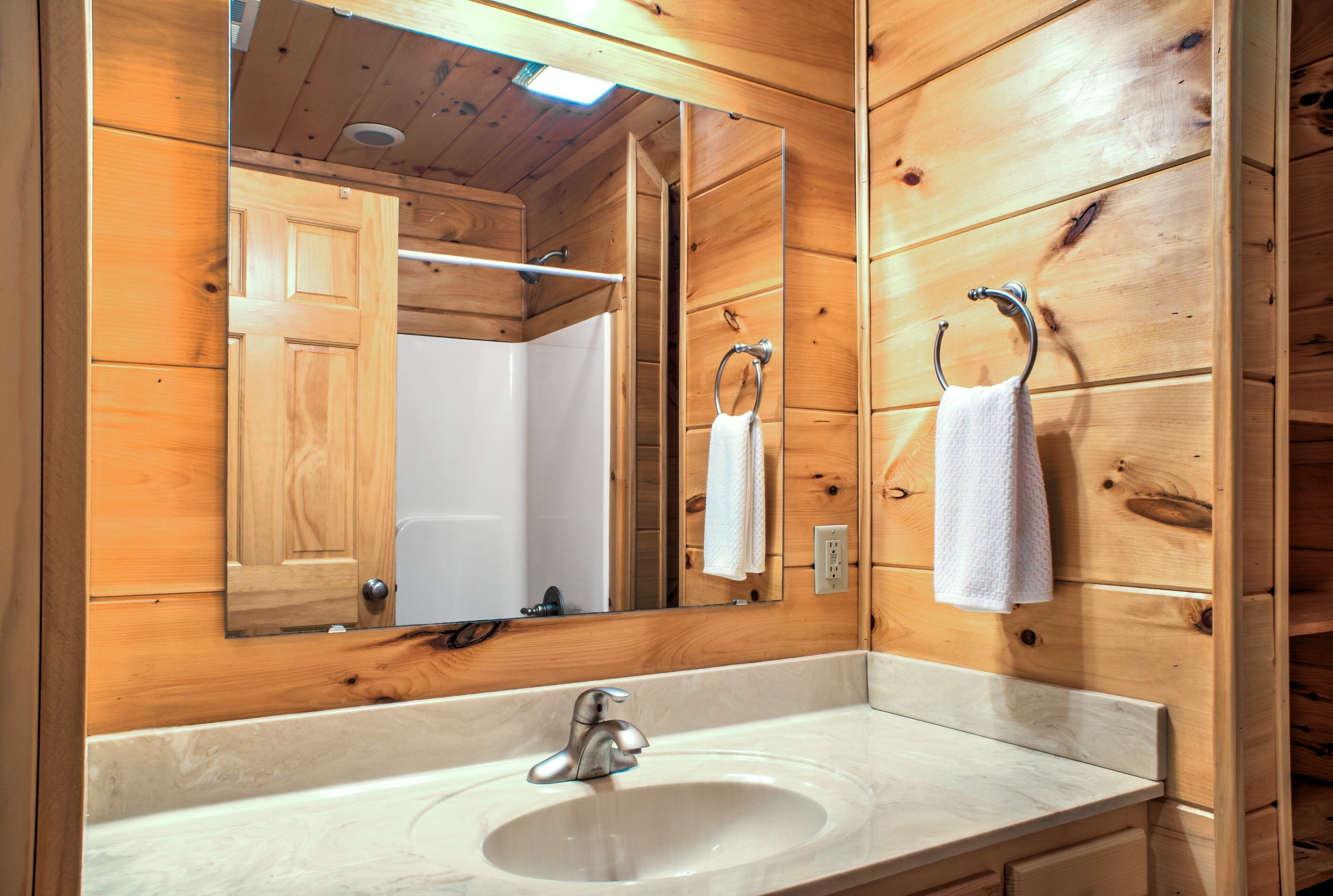 A wooden cabin bathroom with a sink, mirror, towel rack, and wooden walls.