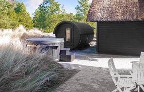 A rustic outdoor seating area with a wooden barrel, a hot tub, and a wooden structure with a thatched roof. - Beautiful home in Rømø with sauna (Rømø)