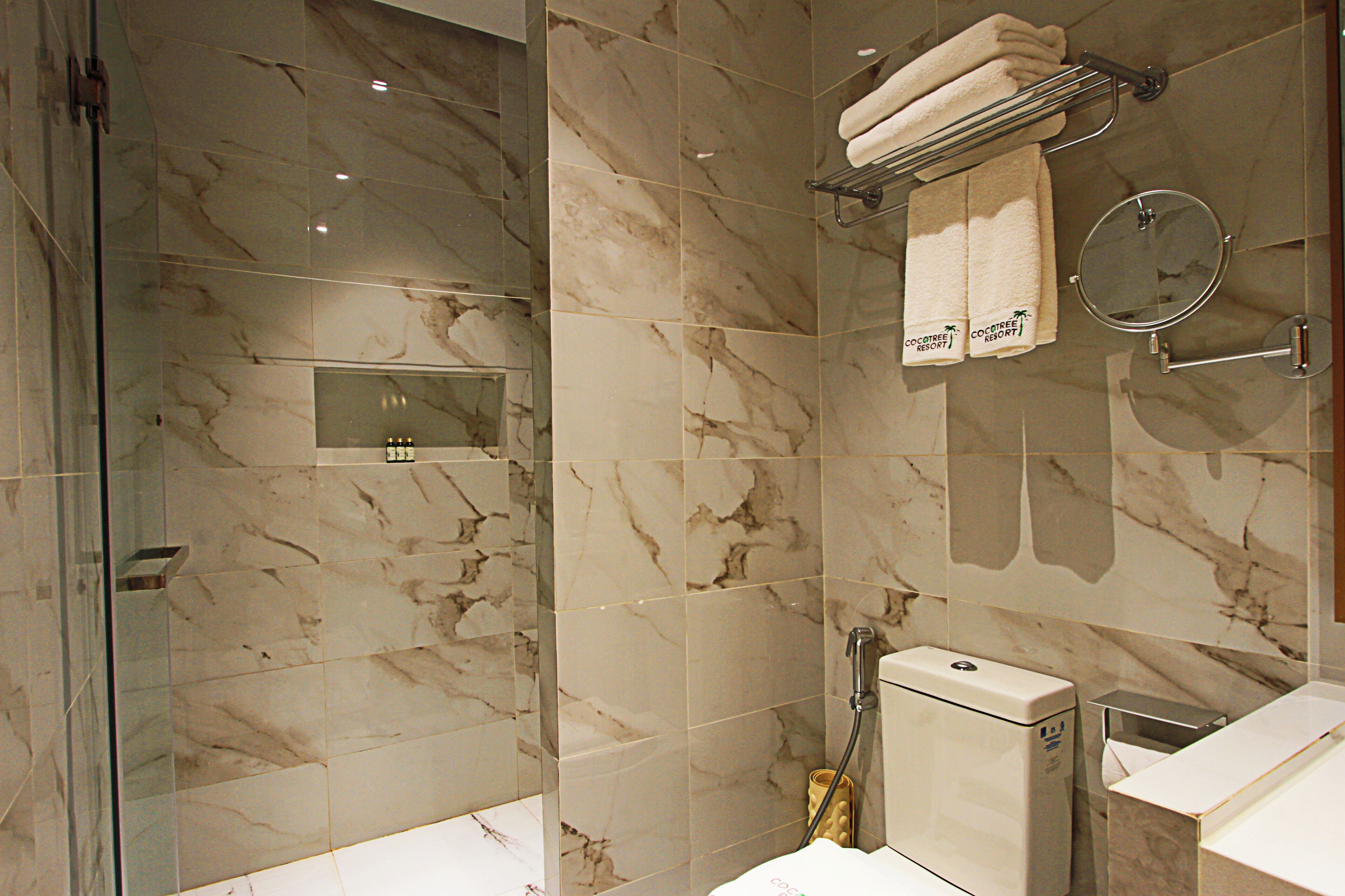 A bathroom with marble tiles, a glass shower enclosure, a towel rack with towels, a toilet, and a bidet.