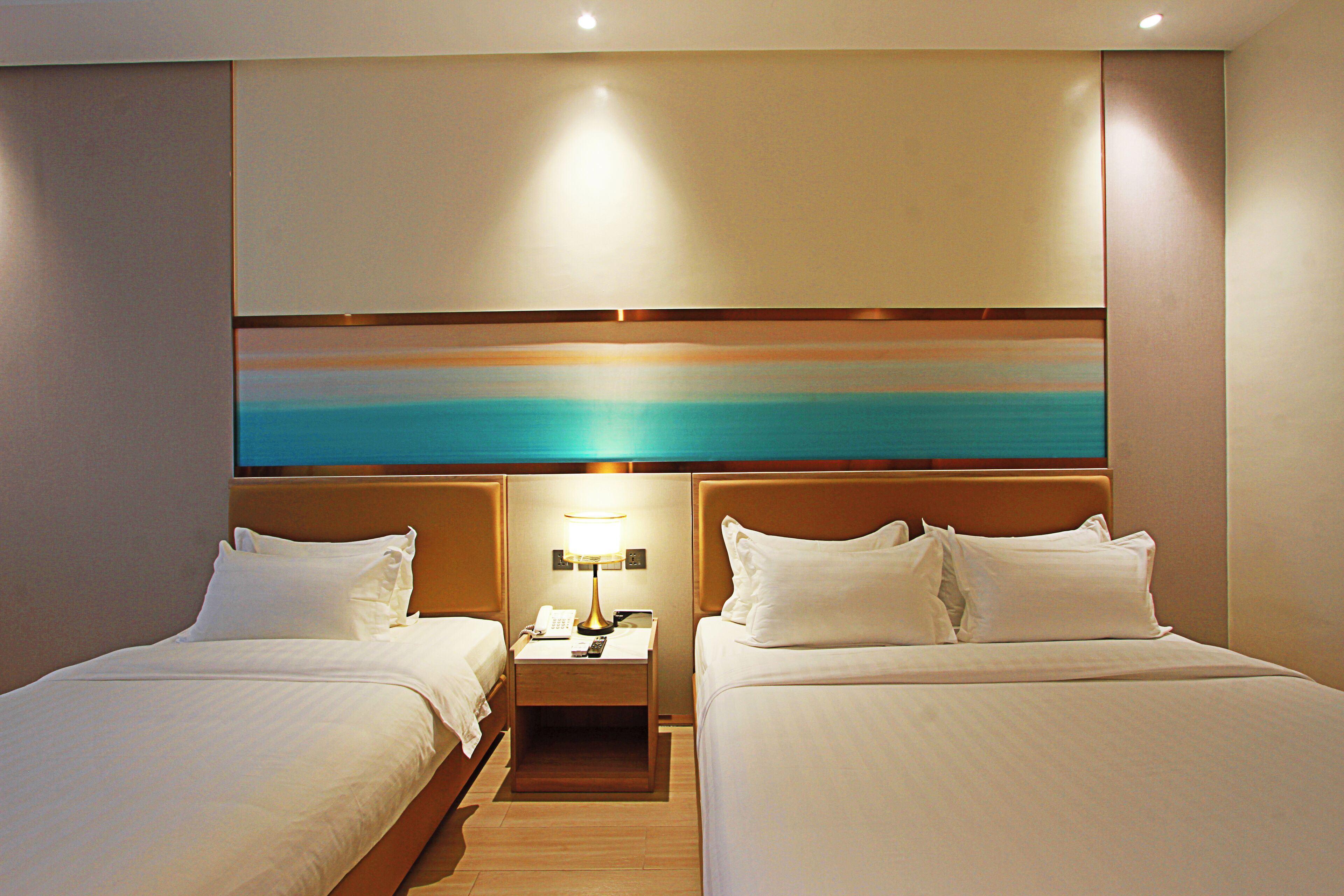 A hotel room with two beds, a nightstand with a lamp, and a large painting above the beds.