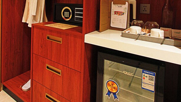A wooden cabinet with a robe hanging on the door, a radio, a refrigerator, and a bottle on the counter. - Cocotree Resort Panglao (Panglao)