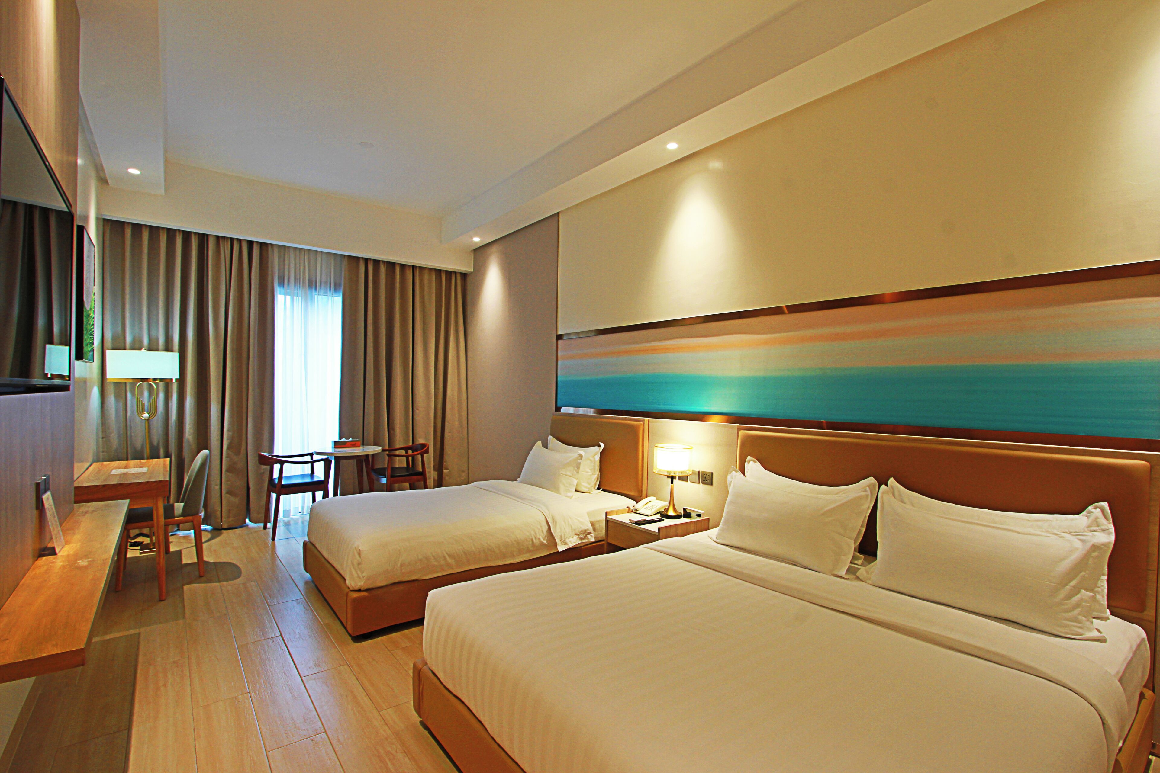 A hotel room with two beds, a desk, a chair, and a small table.