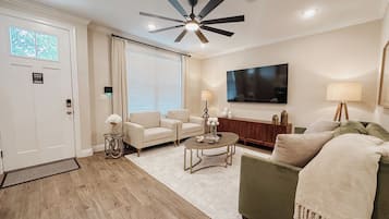 Un salon moderne doté d’un ventilateur de plafond, d’un grand téléviseur à écran plat et d’un canapé vert.