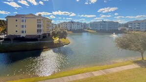 Vista de un lago con zona residencial de edificios de varios pisos, cielo despejado y una fuente.