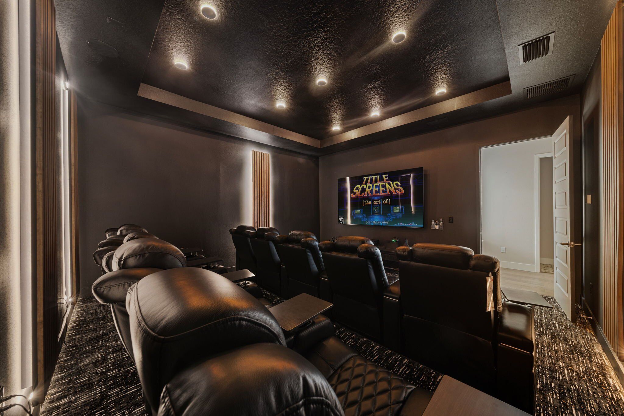 Una sala de cine en casa con sillones de cuero reclinables, un televisor de pantalla plana grande y piso alfombrado.