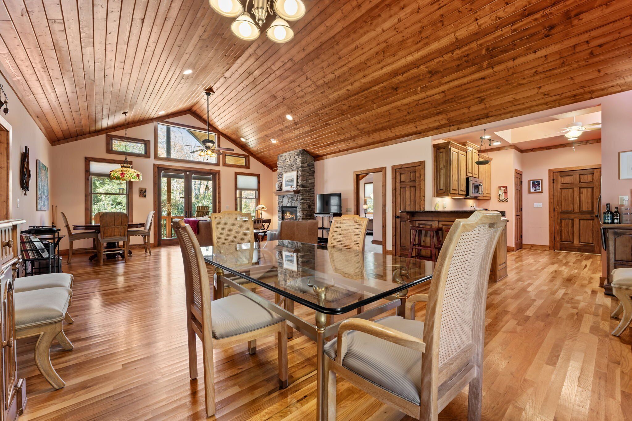 A spacious dining area with a glass-top table and wooden chairs, a kitchen with wooden cabinets, and a stone fireplace.
