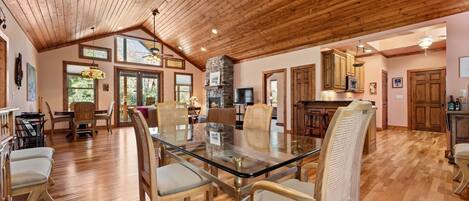 A spacious dining area with a glass-top table and wooden chairs, a kitchen with wooden cabinets, and a stone fireplace.