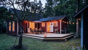 Ein zweigeschossiges Haus mit einer überdachten Terrasse, einem Essbereich und einer kleinen, durch die offene Tür einsehbaren Küche.
