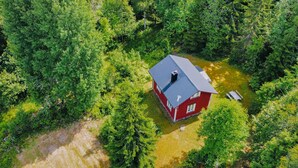 An aerial view of a red house surrounded by dense green forest.