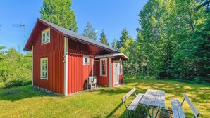 A red wooden house with a small porch and a table and chairs in front.