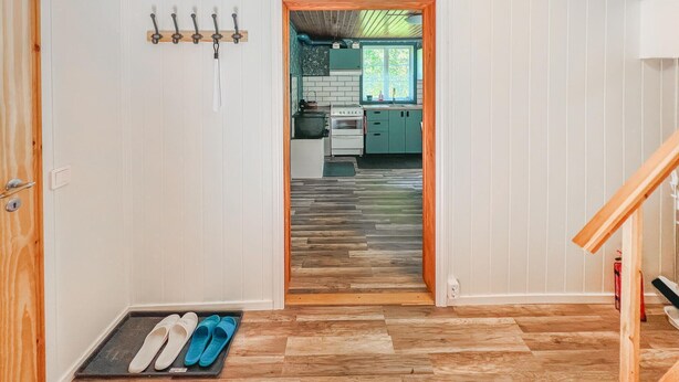 A hallway leading to a kitchen with a wooden floor, a coat rack, and a pair of slippers on a mat.