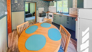 A compact kitchen with a dining area, featuring a wooden table with blue placemats, a refrigerator, and a window providing natural light.
