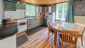 A compact kitchen with a stove, sink, and microwave. There is a dining table with chairs and a window with curtains.