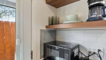 Una cocina con microondas, cafetera y estante de madera con vajilla.
