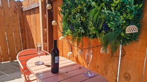 Um pátio externo com mesa e cadeiras de madeira, uma garrafa de vinho e um copo de vinho sobre a mesa.