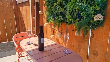 Een terras buiten met een houten tafel en stoelen, een fles wijn en een glas wijn op de tafel.
