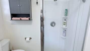 Un baño con ducha de vidrio, inodoro y armario gris con toallas.