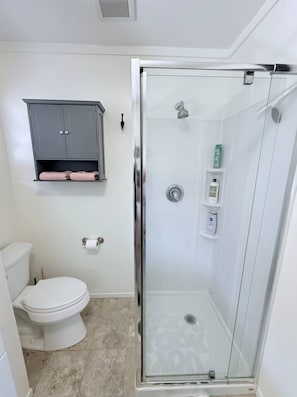 A bathroom with a glass-enclosed shower, a toilet, and a grey cabinet with towels.