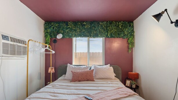 Quarto com cama, luminária de cabeceira e janela com persianas.