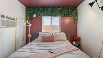 Een slaapkamer met een bed, bedlampje en een raam met zonwering.