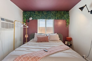 A bedroom with a bed, bedside lamp, and a window with blinds.
