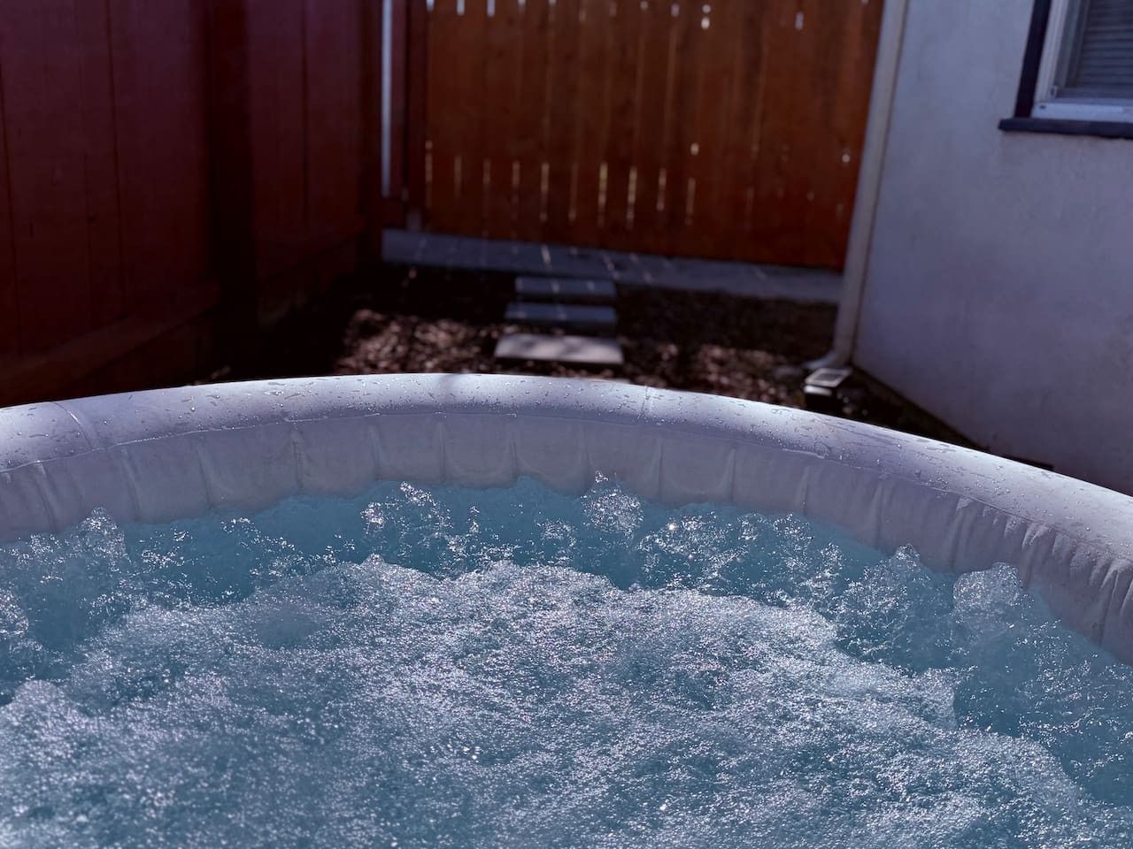 Una bañera de hidromasaje inflable con agua salpicando, rodeada por una valla de madera y una casa.