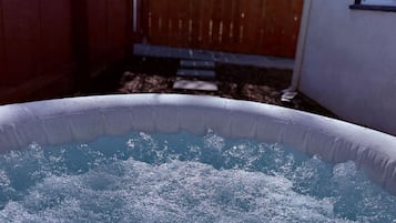 Una bañera de hidromasaje inflable con agua salpicando, rodeada por una valla de madera y una casa.