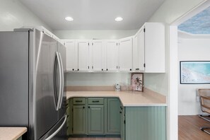 Una cocina con armarios blancos, un refrigerador de acero inoxidable y una encimera de color claro.