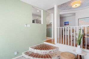 A staircase with a brick design leading to a room with a white railing and a plant on a small table.
