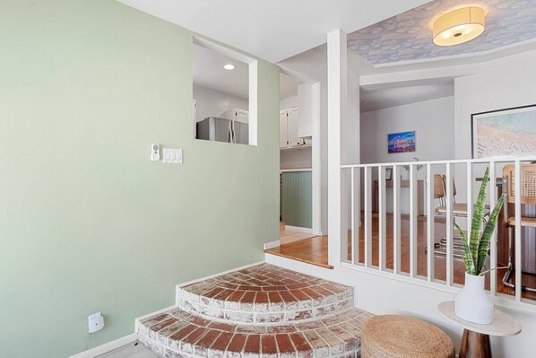 Una escalera de ladrillo conduce a un espacio con barandilla blanca y una planta sobre una mesita.