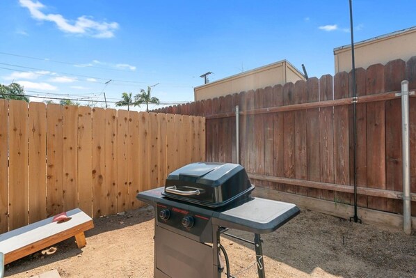 A portable barbecue grill with a control panel, a wooden bench, and a wooden fence in a backyard setting.