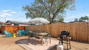 Un jardin avec une clôture en bois, du mobilier d’extérieur, un barbecue et une bouteille de gaz.