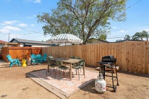 Een achtertuin met een houten omheining, tuinmeubilair, een barbecue en een gasfles.