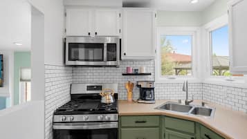 A modern kitchen with white cabinets, a stainless steel microwave, a gas stove, and a coffee maker.