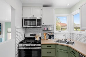 Una cocina moderna con armarios blancos, un microondas de acero inoxidable, una estufa a gas y una cafetera.
