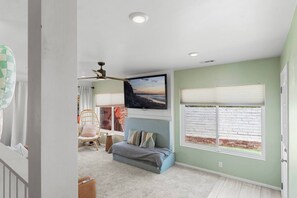Una habitación con cama, una silla, ventana con persianas, ventilador de techo y un cuadro en la pared.