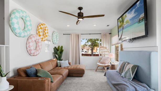 Un salon avec un canapé en cuir marron, un canapé bleu, un ventilateur de plafond et une grande fenêtre donnant sur une plage.