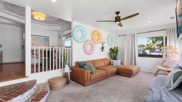 A spacious living room with a brown leather sofa, a ceiling fan, and a view of the outside through a large window.