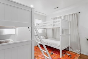 Habitación con literas, ventana, paredes blancas y alfombra estampada.