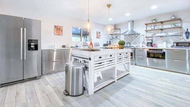 A modern kitchen with stainless steel appliances, a central island with drawers, pendant lighting, and a trash bin. - LUX 7BR/4BA Villa w/Heated Pool, next to the Strip (Las Vegas)